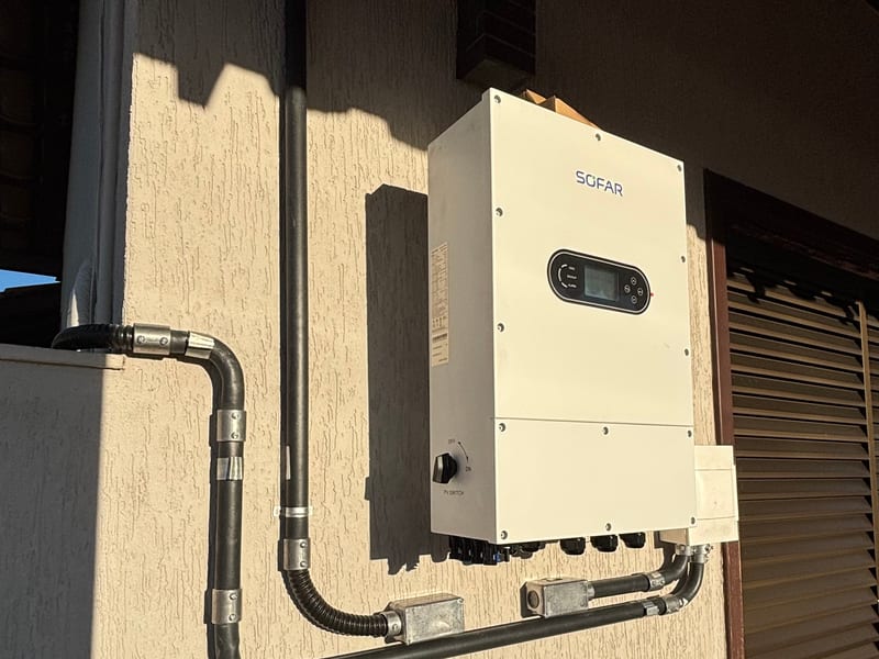 Inversor híbrido instalado em parede externa, com eletrodutos e módulos fotovoltaicos ao lado