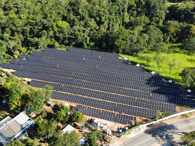 Usina fotovoltaica em estrutura de solo, instalada em encosta ao lado de área de mata